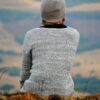 person in gray sweater sitting on green grass overlooking mountian